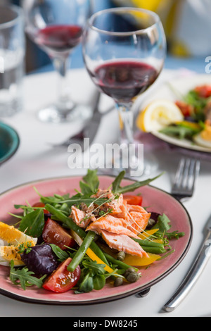 Salat mit Lachs und Verdure in rosa Platte auf Tisch mit blauer Stuhl Hintergrund Stockfoto