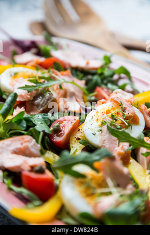 Salat mit Lachs, Gemüse und Grün in rosa Platte auf Retro-Zeitung Hintergrund Stockfoto