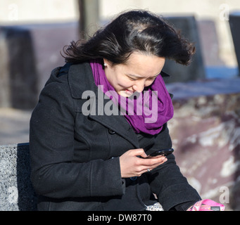 Junge Frau sitzen außen SMS auf ihr Handy. Stockfoto