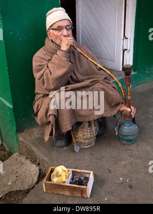 Indien, Kaschmir, Srinagar, Mann tragen Kashmiri Phiren Mantel Rauchen Shisha Wasserpfeife außerhalb im winter Stockfoto