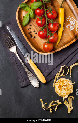 Tomaten auf der Rebe, Basilikum und gelb Chili serviert auf hölzerne Schüssel Stockfoto