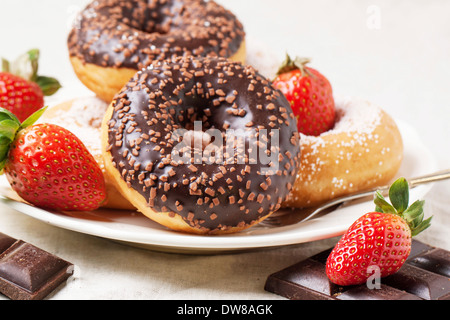 Platte mit Schokoladen Donuts, frischen Erdbeeren und dunkle Schokolade serviert auf grau Textil Stockfoto