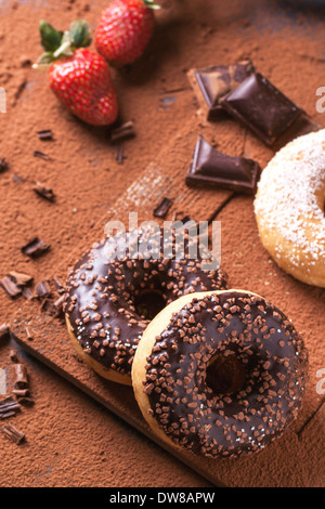 Schokoladen Donuts mit frischen Erdbeeren und dunkle Schokolade serviert auf Schneidebrett mit Kakaopulver als Hintergrund. Stockfoto