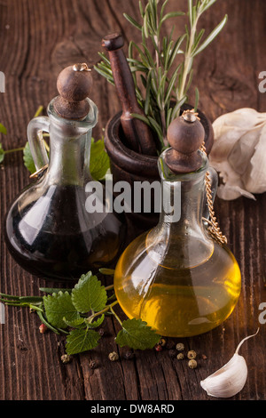 Draufsicht auf Olivenöl und Essig in Vintage-Flaschen auf Holztisch mit Knoblauch, Minze und Rosmarin in hölzernen Mörser Stockfoto