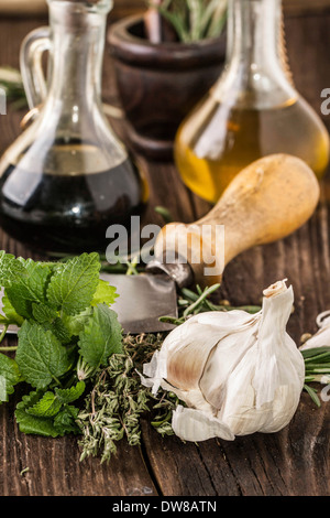 Vintage Messer mit Knoblauch, Minze und Thymian, Öl und Essig in Vintage-Flaschen auf alten Holztisch Stockfoto