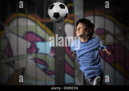 Ein kleiner Junge spielt Streetsoccer Wand Graffiti bedeckt - dramatische Beleuchtung und gedämpften Farben Stockfoto