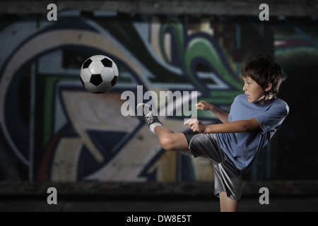 Ein kleiner Junge spielt Streetsoccer Wand Graffiti bedeckt - dramatische Beleuchtung und gedämpften Farben Stockfoto