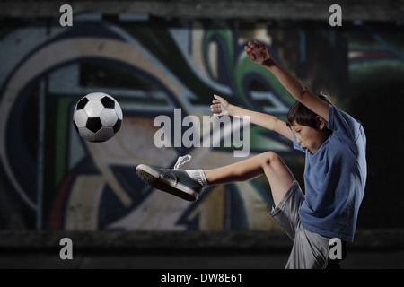 Ein kleiner Junge spielt Streetsoccer Wand Graffiti bedeckt - dramatische Beleuchtung und gedämpften Farben Stockfoto