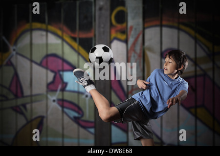 Ein kleiner Junge spielt Streetsoccer Wand Graffiti bedeckt - dramatische Beleuchtung und gedämpften Farben Stockfoto