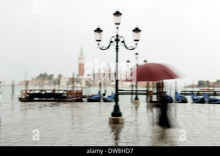 Italien, Venedig, Frau wandern im Regen auf Riva degli Schiavoni mit Blick über San Giorgio Maggiore Stockfoto