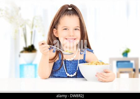 Niedliche kleine Mädchen essen Müsli aus einer Schüssel sitzt zu Hause auf Tisch Stockfoto