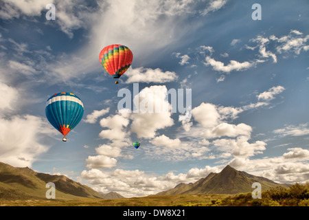 Drei heiße Luftballons fliegen über Bergwildnis in Kanada mit geschwollenen Wolken und blauer Himmel. Stockfoto