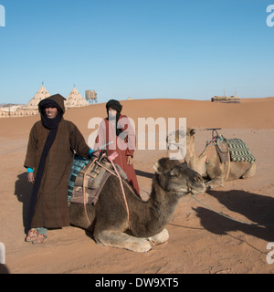 Zwei Tuareg-Männer stehen in einer Wüste mit ihren Kamelen, Erg Chigaga Luxus Desert Camp, Wüste Sahara, Marokko Stockfoto