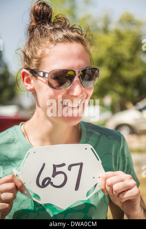 Junge weibliche Mountainbiker Startnummer hochhält Stockfoto