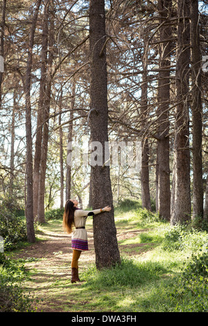 Junge Frau umarmt Baumstamm im Wald Stockfoto