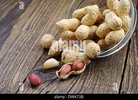 Erdnüsse in Glas Schüssel geben und in der Nähe auf hölzernen Hintergrund Stockfoto