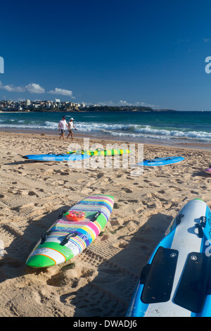 Männliche Steyne Nordstrand mit Surfbrettern im Vordergrund und paar zu Fuß entlang der Küste Sydney New South Wales NSW Australia Stockfoto