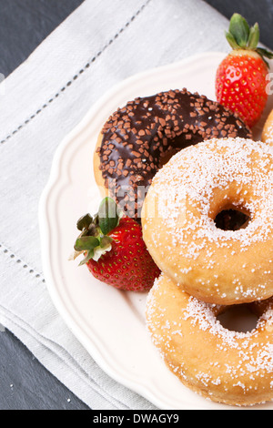 Weißer Teller von Schokolade und Zucker Donuts und frischen Erdbeeren serviert auf grau Textil Serviette über schwarzen Tisch. Stockfoto