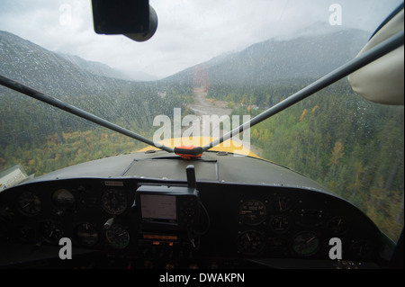 Fahrgastsicht eines einmotorigen Flugzeug fliegen durch ein Bergtal unter Wolken und regnerischem Wetter Stockfoto