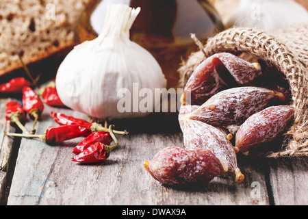 Wenig Salami in ein Säckchen mit red hot Chili Peppers und Knoblauch über alten Holztisch. Stockfoto