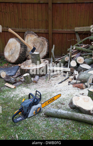 Eine Axt in einem Stück Holz auf einem Hackblock und eine Ryobi Kettensäge für die Herstellung von Brennholz, England, UK Stockfoto