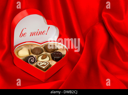 Pralinen in goldenes Herz-Form-Box über rote Seide Hintergrund. Valentinstag Geschenk mit Beispieltext BE MINE! Stockfoto