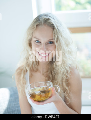 Porträt der glückliche junge Frau hält Kräuterteetasse im Haus Stockfoto