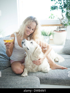 Schöne Frau mit Teetasse beim Berühren Hund auf sofa Stockfoto