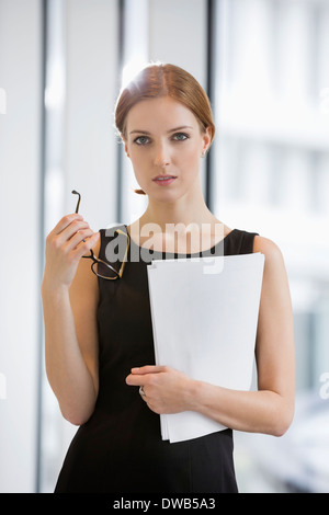 Porträt von zuversichtlich Geschäftsfrau hält Dokumente und Brillen im Büro Stockfoto