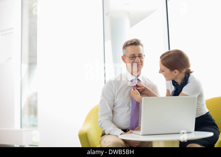 Geschäftsfrau aufsetzen Krawatte an männlichen Kollegen in der lobby Stockfoto