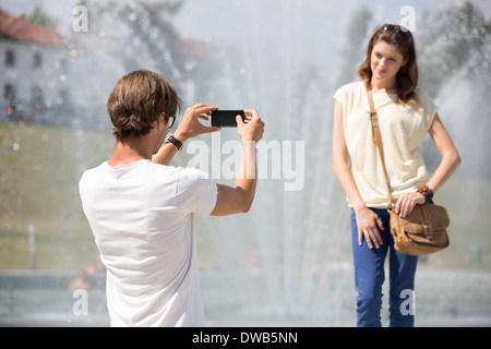 Junger Mann fotografiert Frau gegen Brunnen Stockfoto