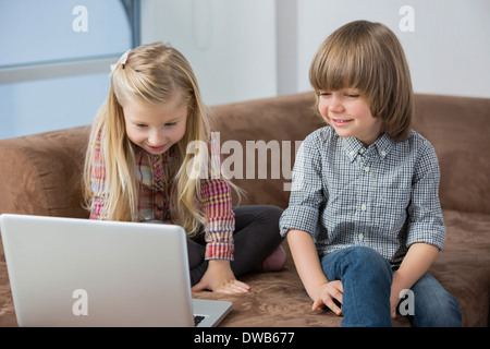 Fröhlicher Junge mit Schwester mit Laptop auf sofa Stockfoto