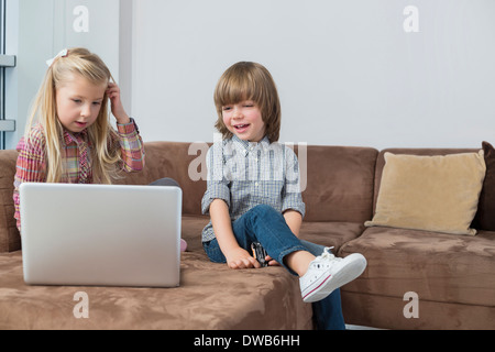 Fröhlicher Junge mit Schwester mit Laptop auf sofa Stockfoto
