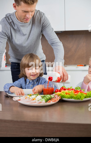 Vater Gießen Saft für Sohn am Tisch in der Küche Stockfoto