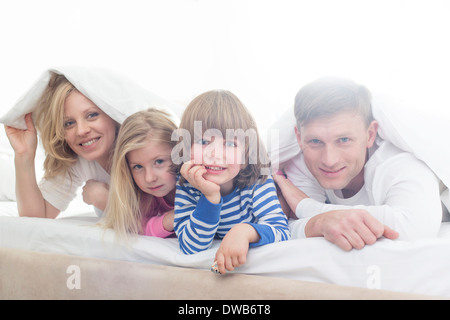 Porträt von glücklichen Eltern und Kinder unter der Bettdecke liegen Stockfoto