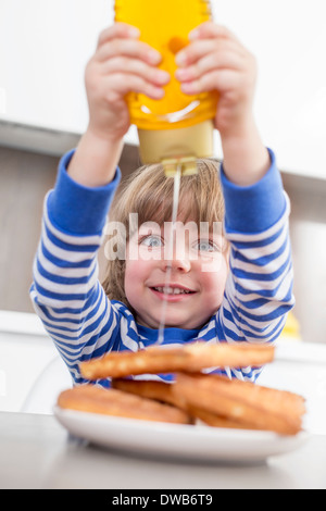 Fröhlicher Junge Gießen Honig auf Waffeln zu Hause Stockfoto
