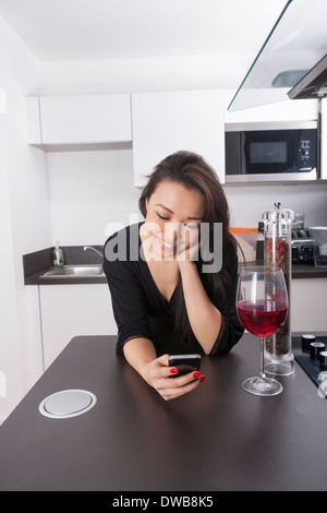 Glückliche junge Frau lesen SMS auf smart Phone in Küche Stockfoto