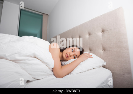 Nachdenkliche junge Frau im Bett liegend Stockfoto
