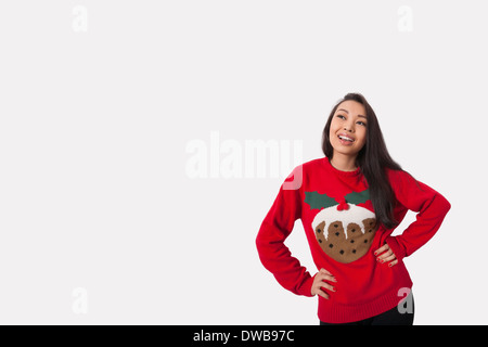 Junge Frau in Weihnachten Pullover ansehen mit Hände auf den Hüften auf grauem Hintergrund Stockfoto