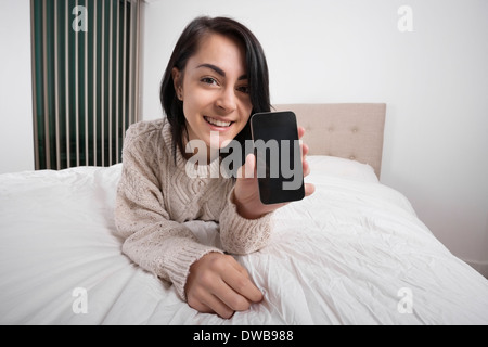 Porträt der glückliche Frau zeigt Smartphone beim liegen im Bett Stockfoto