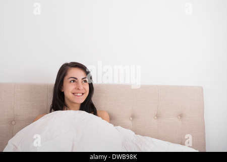 Nachdenkliche junge Frau lächelnd im Bett Stockfoto