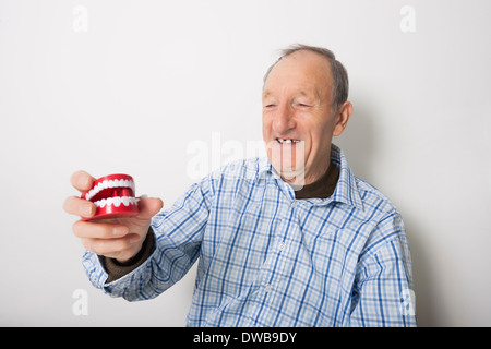 Senior glücklich halten Prothesen vor grauem Hintergrund Stockfoto