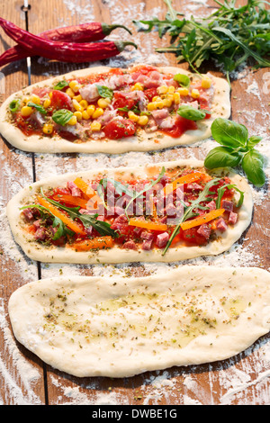 Rohen Pizzateig mit Schinken, Käse, Tomaten, Rucola, Mais, Paprika,, Knoblauchöl und Basilikum Stockfoto