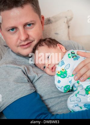 Porträt von 1 Monat alt baby jungen in seinem Papa Armen, fast eingeschlafen zu Hause. Stockfoto