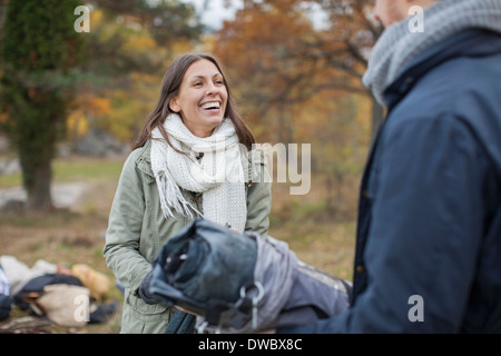 Glückliche Frau im Winterjacke und Schal Blick auf Menschen während camping Stockfoto