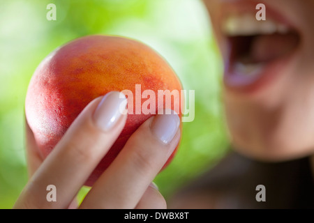 Frau Holding Pfirsich in den Mund Stockfoto