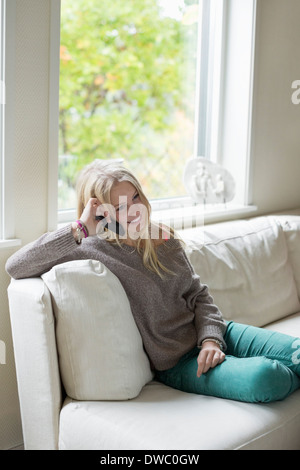 Teenager-Mädchen mit Handy während Sie gemütlich auf dem Sofa zu Hause Stockfoto