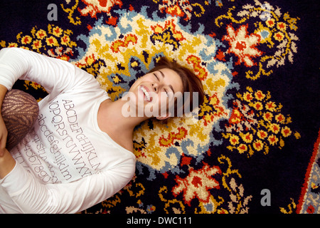 Junge Frau liegend auf gemusterten Teppich vor Lachen Stockfoto