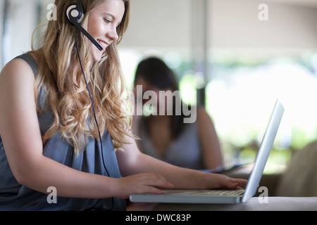 Junge Büroangestellte sprechen über Kopfhörer während auf laptop Stockfoto