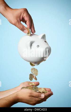 Hand, Münze ins Sparschwein und Münzen heraus fließt Stockfoto